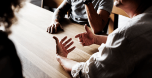 Three people sitting around a table. The image shows their hands.