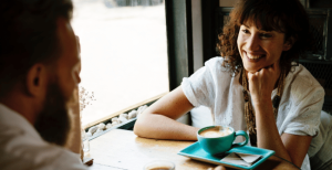 A man and woman sitting opposite each other with coffee in front of them, chatting